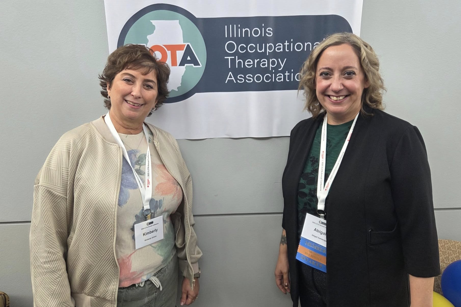 Swidergal wins award from occupational therapy association 2 people smiling at camera while standing in front of wall with small banner.