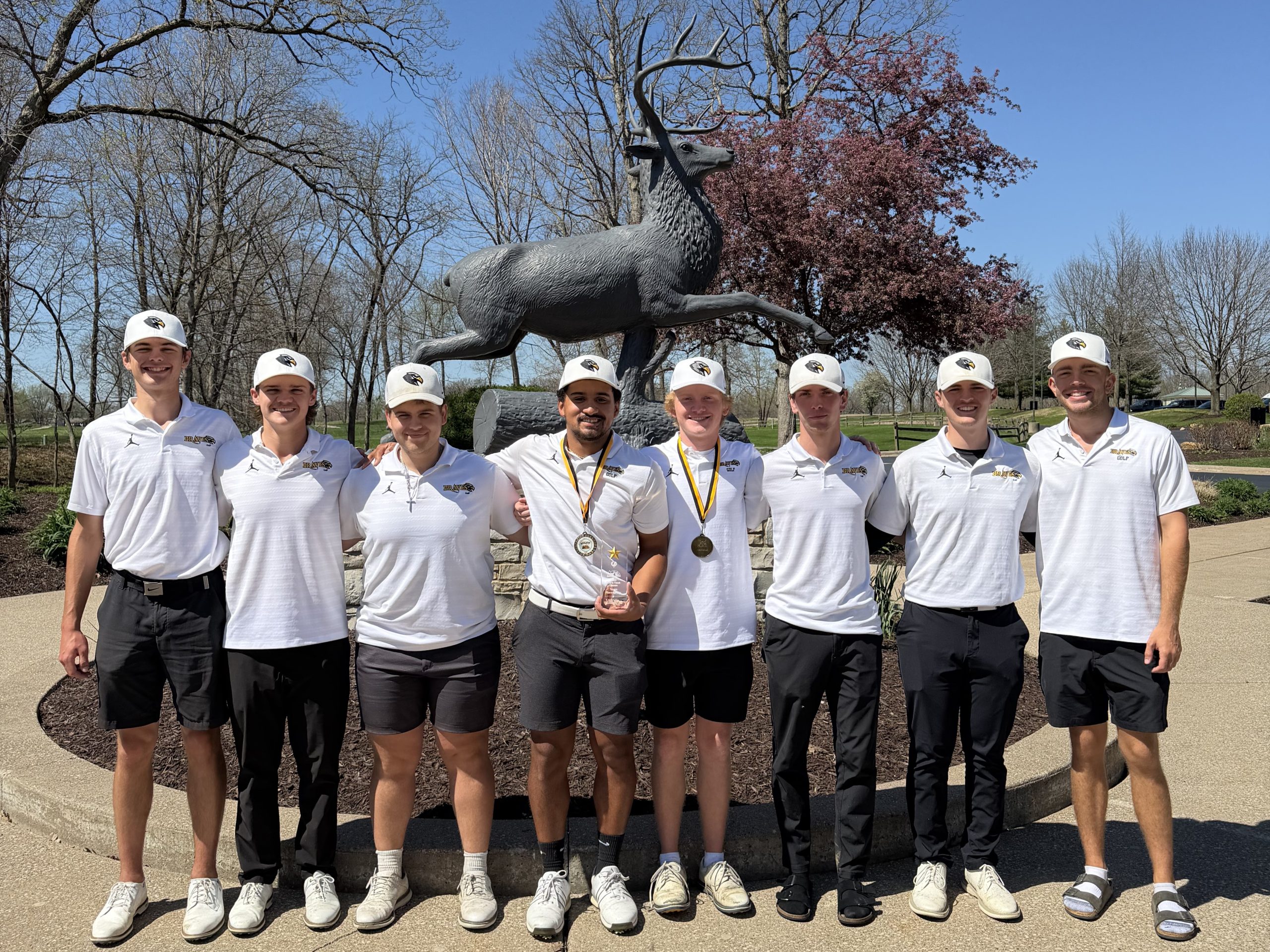 8 golfers standing in front of life-size deer sculpture at tpc deere run golf course.