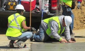 A person in safety vests and white helmets working on a concrete surface