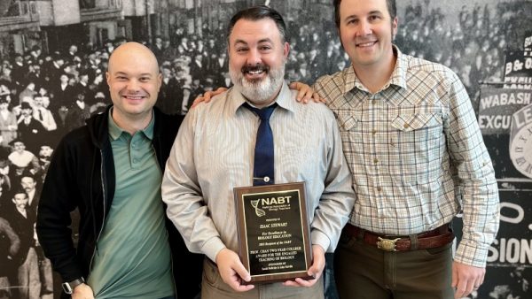 3 people standing and smiling at camera with one holding an award plaque.