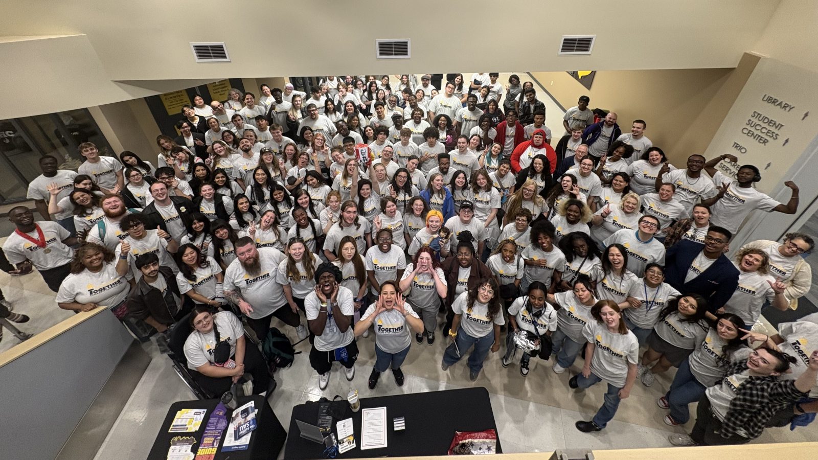 Dozens of happy people standing in a lobby looking up and smiling at the camera.