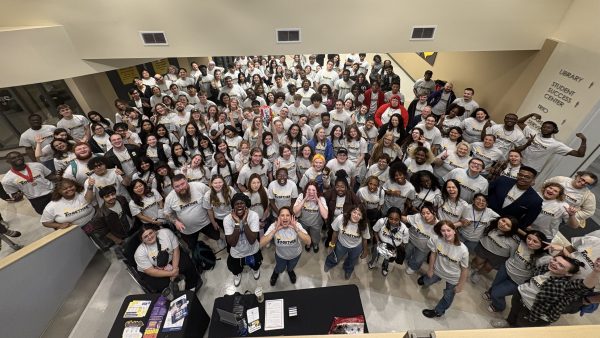 Dozens of happy people standing in a lobby looking up and smiling at the camera.