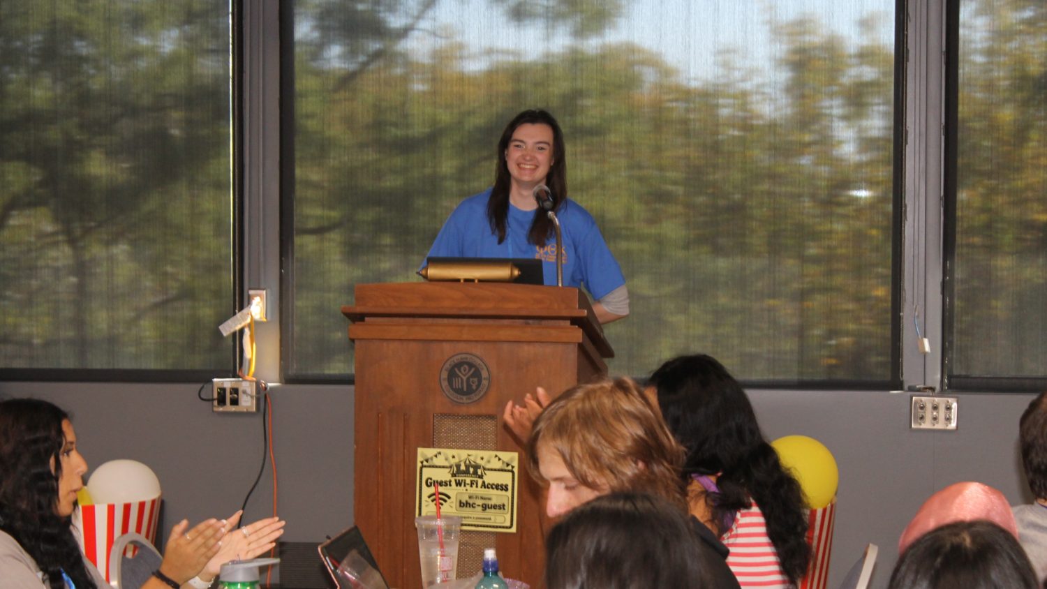 Woman standing at podium talking and smiling.
