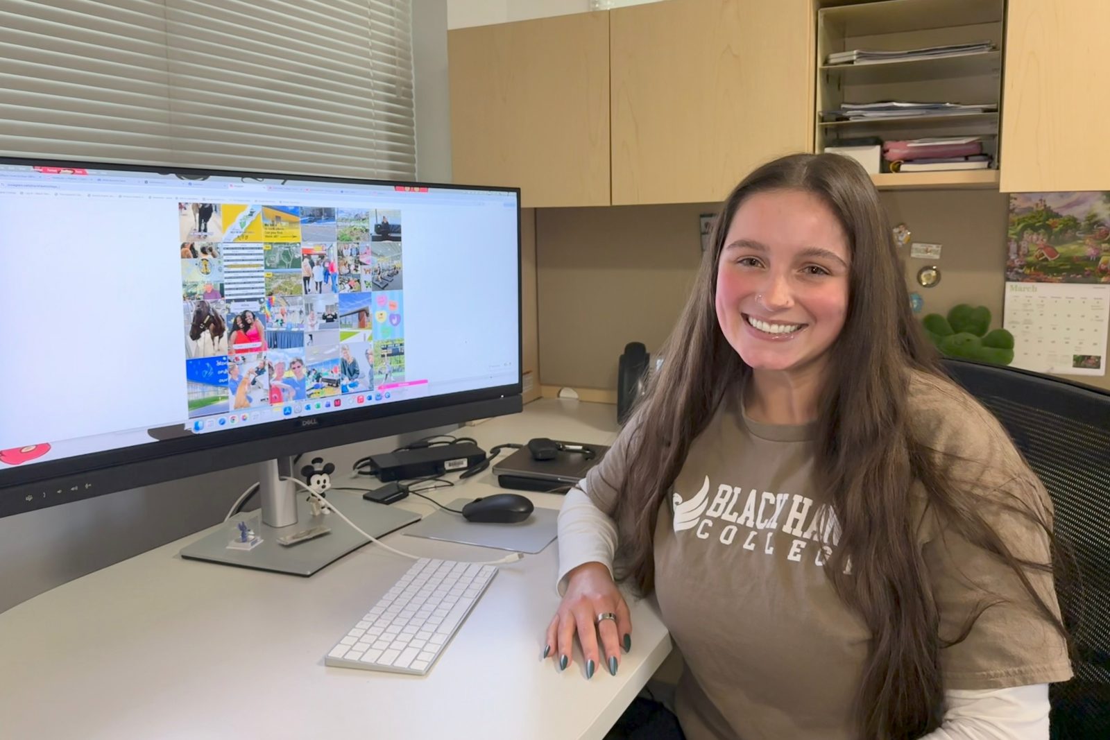 Smiling woman sitting at desk in front of computer monitor.