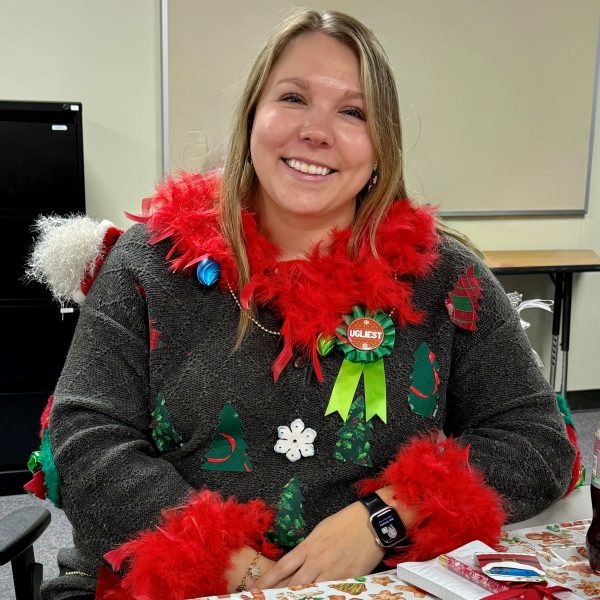 Seated smiling woman wearing ugly christmas sweater.