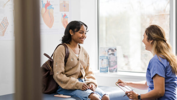 The young adult female patient smiles while listening to the nurse give an encouraging update regarding her medical exam that was recently completed.