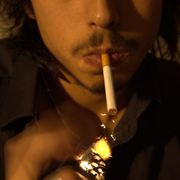 Closeup of man with cigarette in his mouth using lighter to light cigarette.