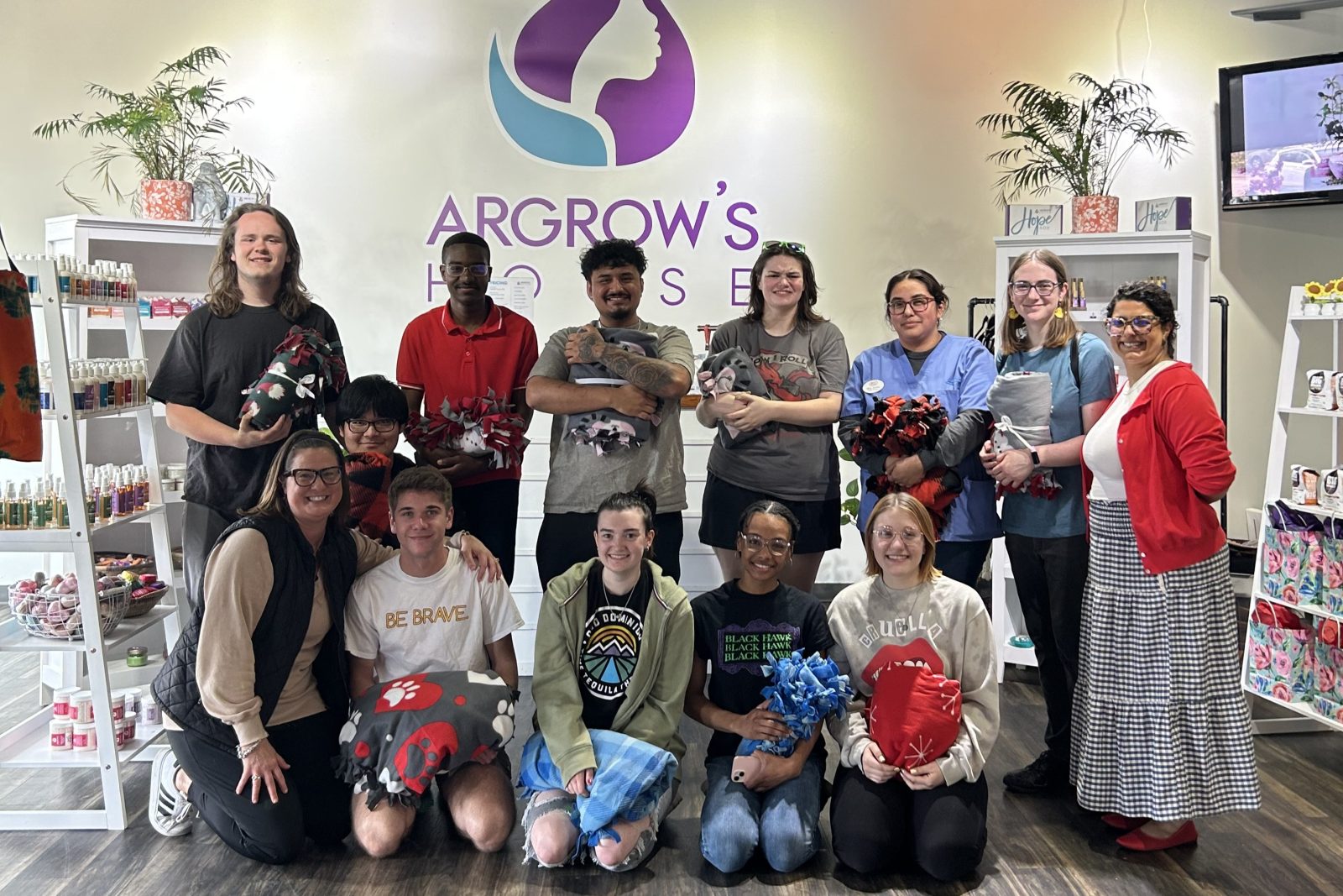 13 people holding tie blankets at argrow's house.