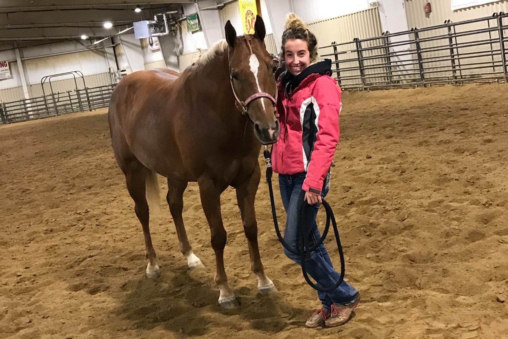 Woman standing with horse in an indoor arena.
