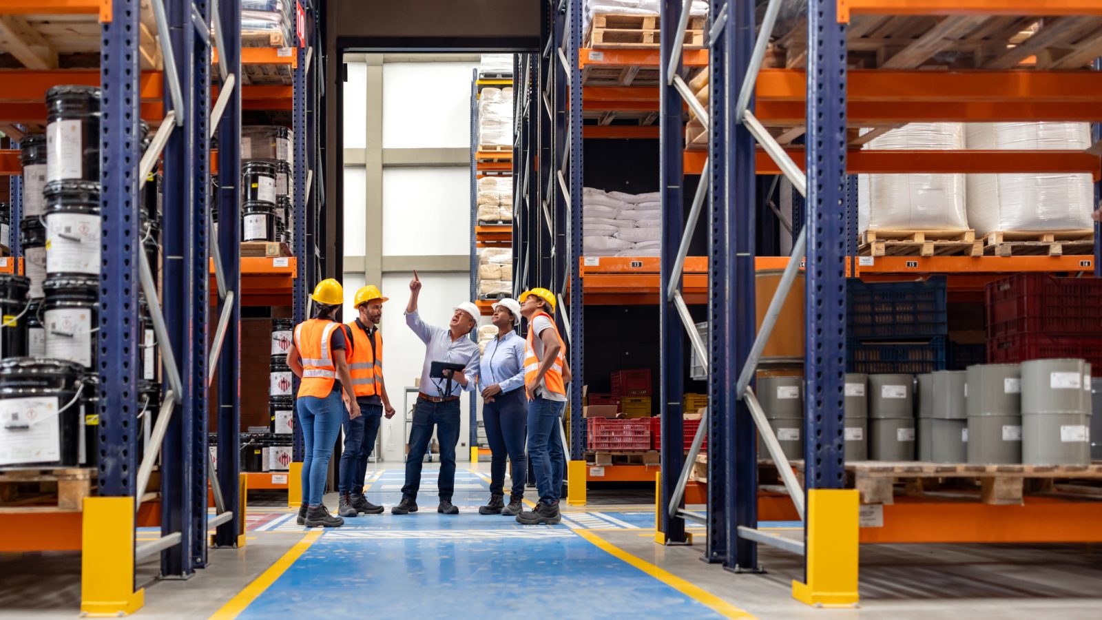 Forperson talking to a group of employees in a meeting at a distribution warehouse and pointing away