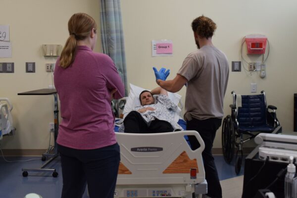 Two health care providers standing by hospital bed talking with patient who is in the bed,