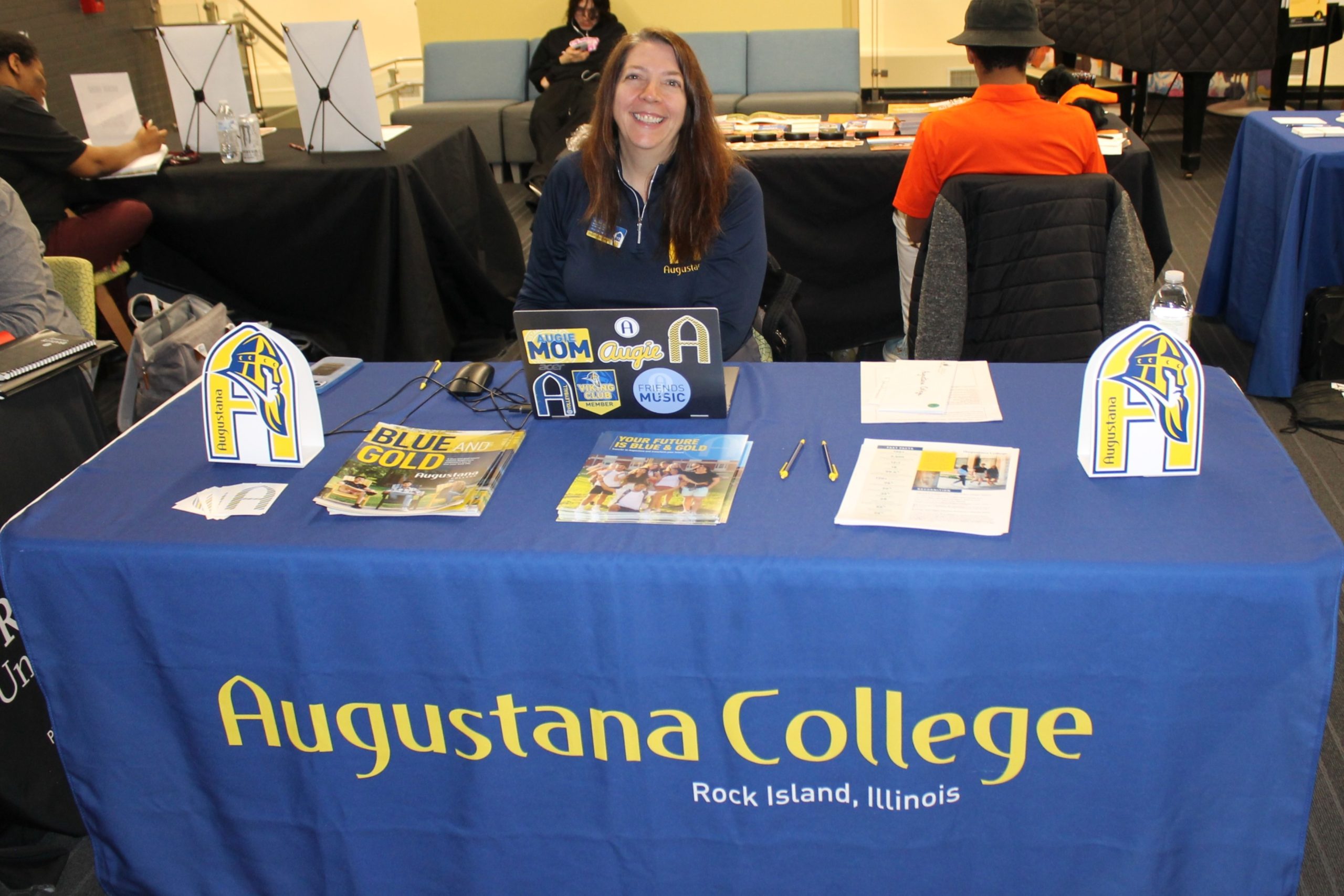Person sitting at table covered by tablecloth and college promotional materials.