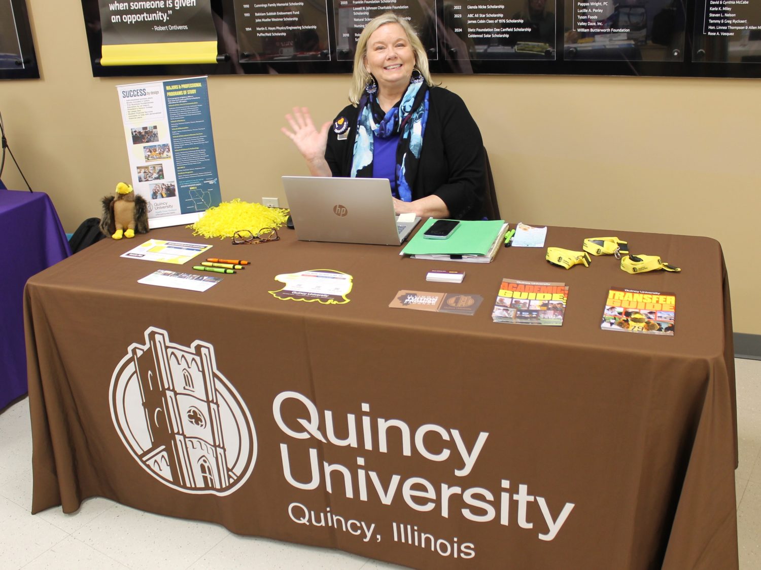 Person sitting at table covered by tablecloth and college promotional materials.