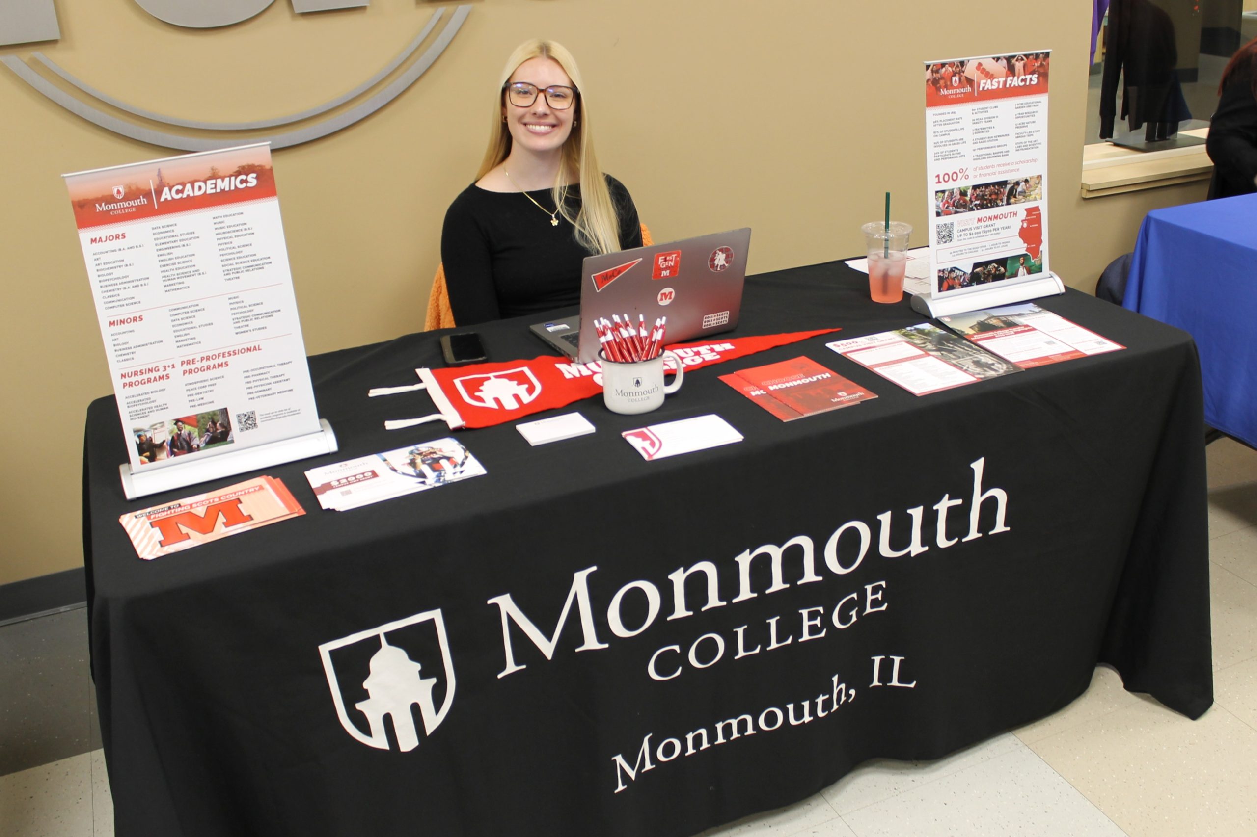 Person sitting at table covered by tablecloth and college promotional materials.