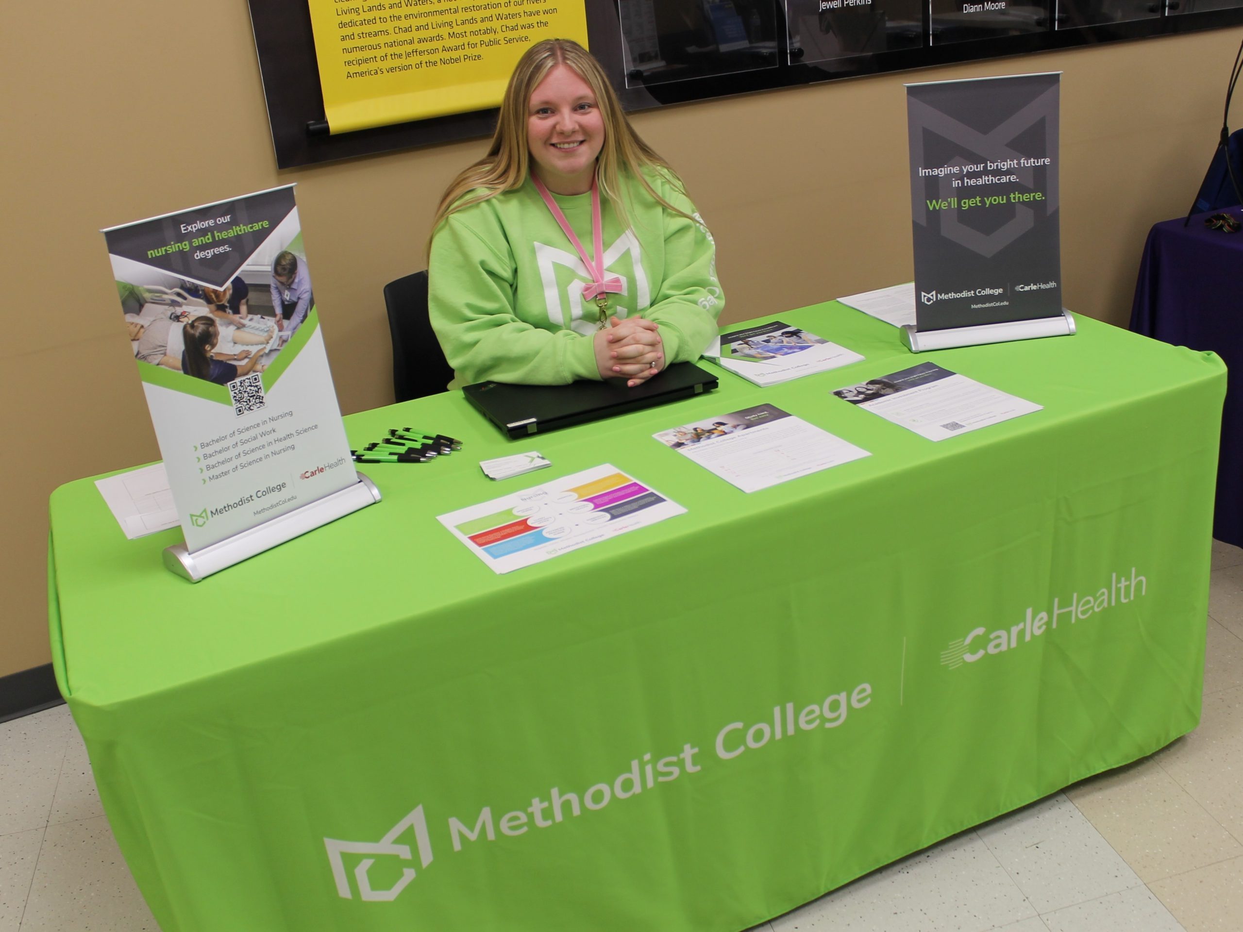Person sitting at table covered by tablecloth and college promotional materials.