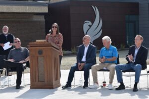 Marybeth stopoulos standing at podium outside building 3 with 4 people seated by podium