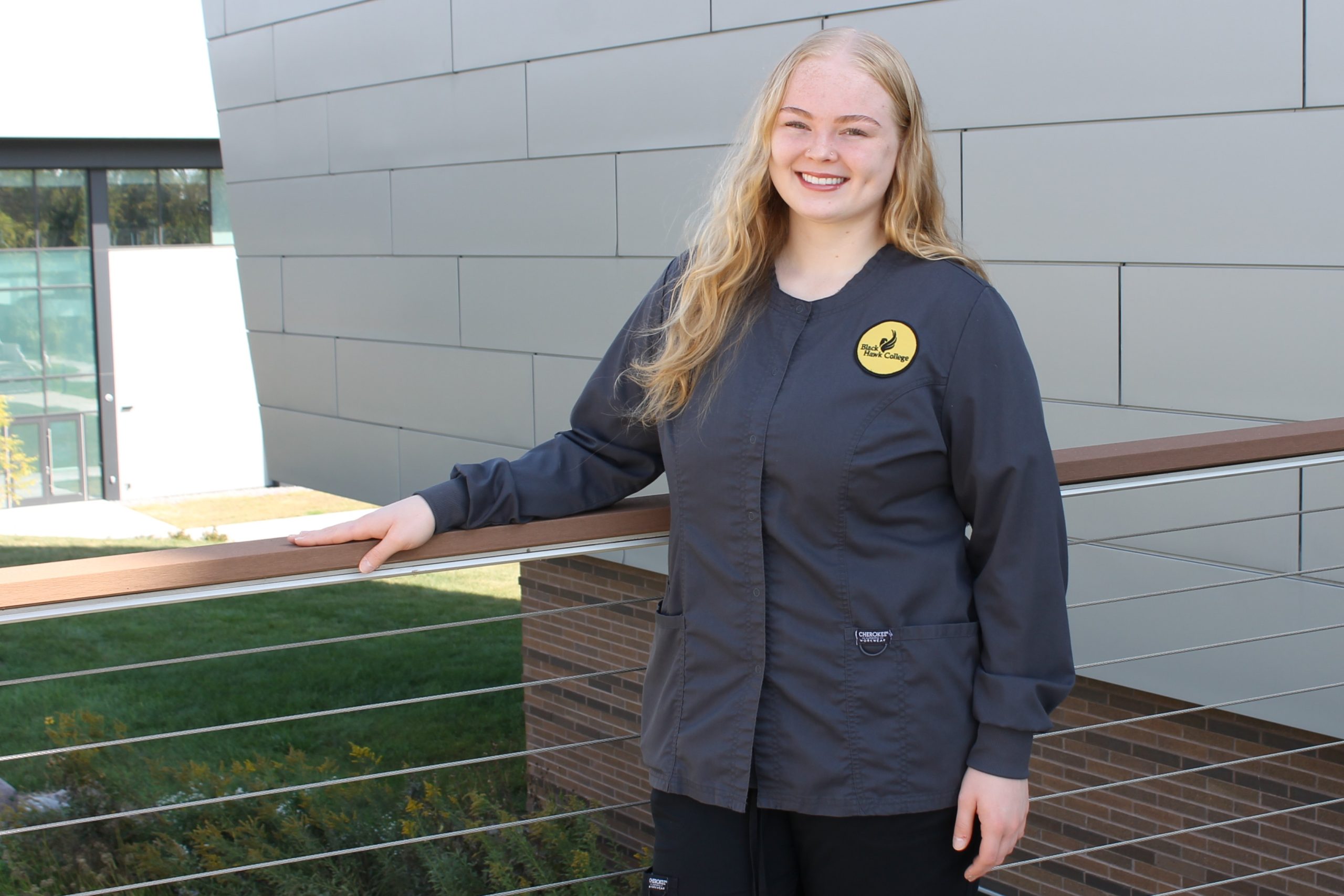 Nursing student in scrubs standing outside health sciences center.