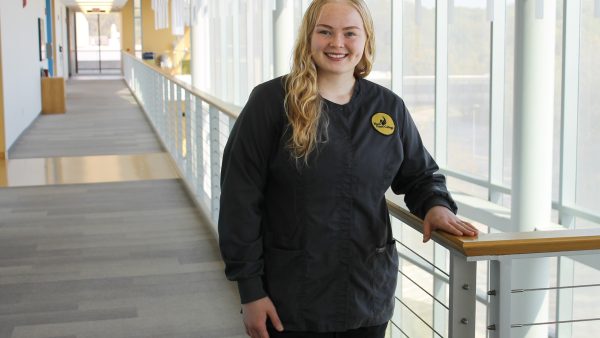 Nursing student in scrubs standing inside health sciences center.
