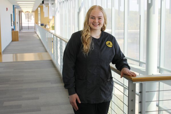 Nursing student in scrubs standing inside health sciences center.