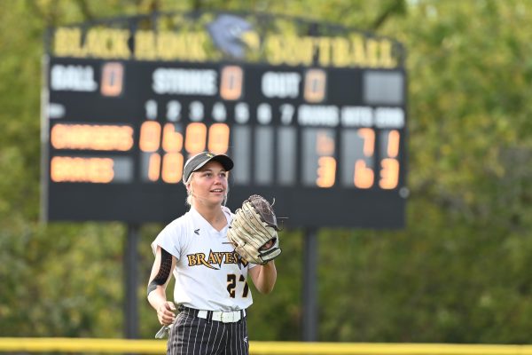 Softball player on field, scoreboard visible.