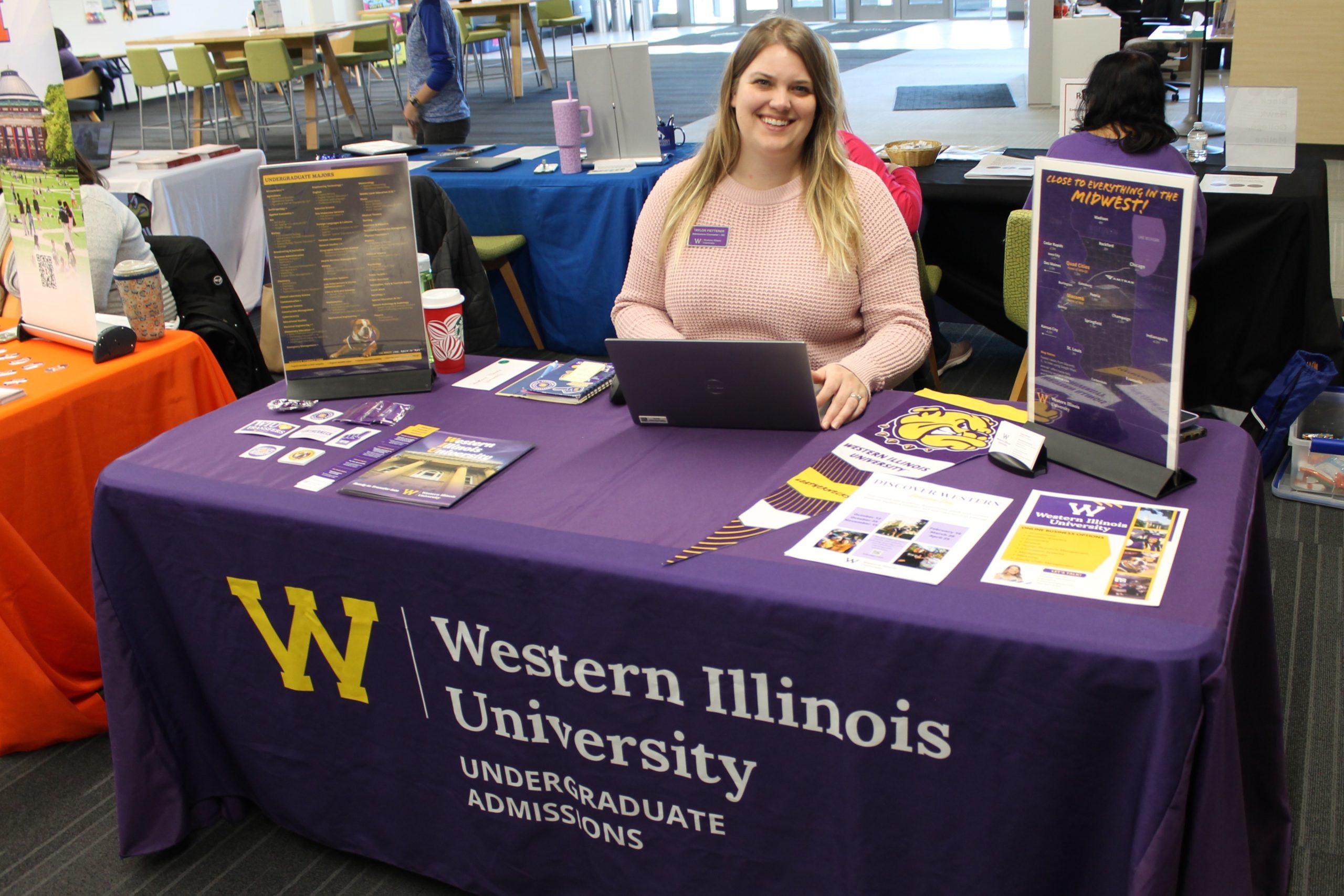 Person sitting at table covered by tablecloth and college promotional materials.