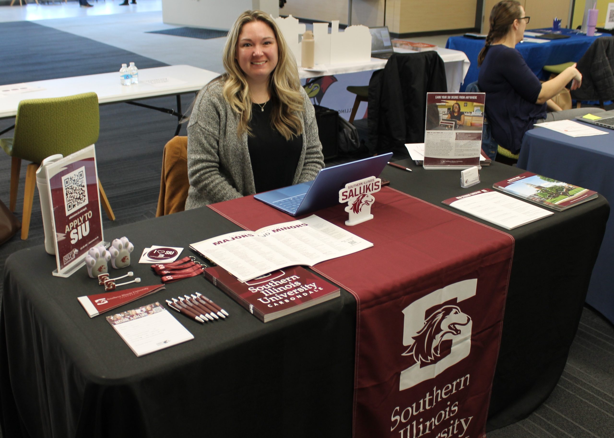 Person sitting at table covered by tablecloth and college promotional materials.