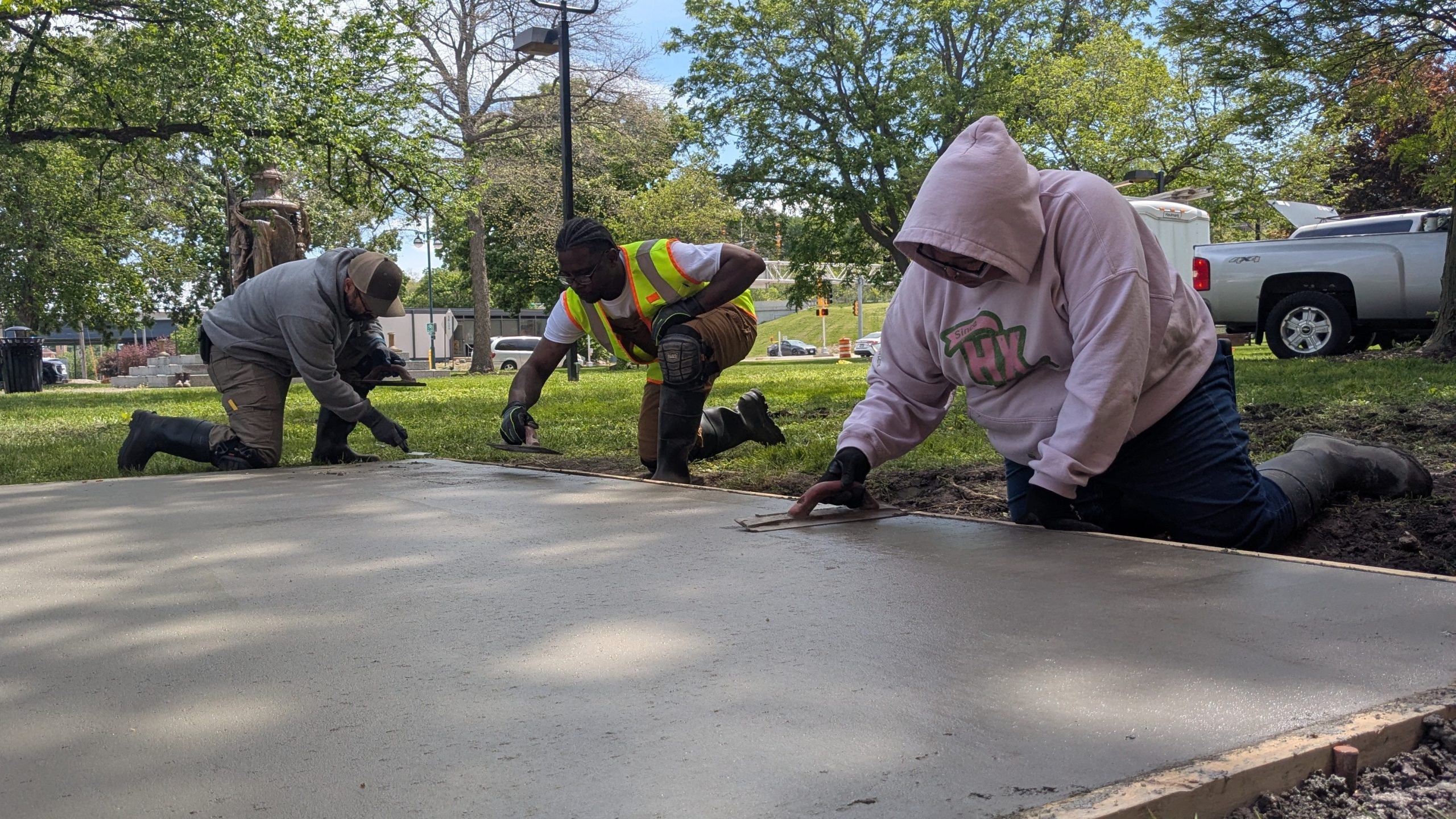 Congratulations to spring 2026 highway construction grads 3 people kneeling and using finishing trowels on slab of concrete.