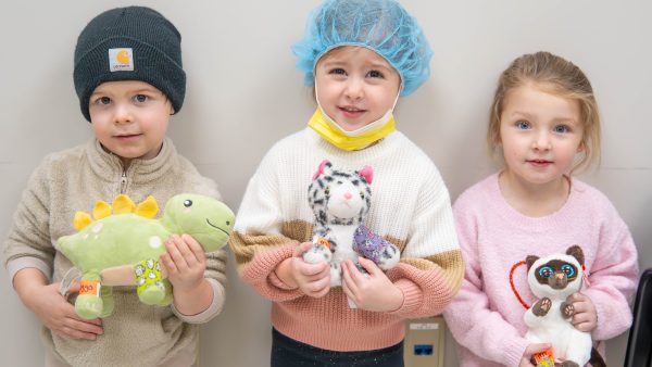 3 children looking at camera and holding stuffed animals.