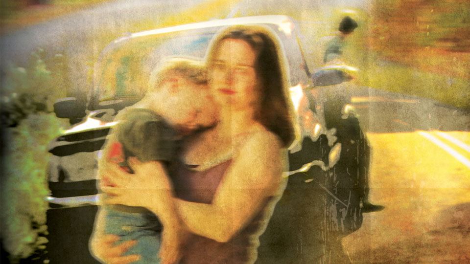 Slightly blurry image of woman holding child in front of a vehicle.