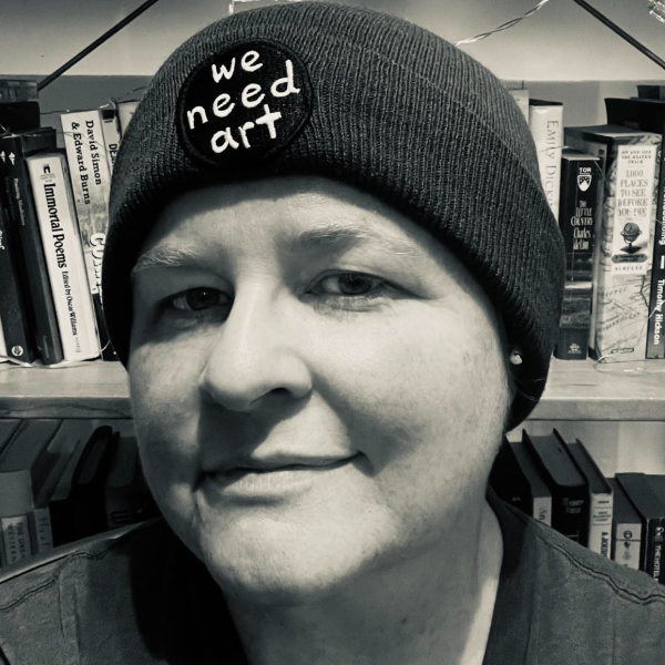 Head shot of person wearing knit hat with words we need art on it.