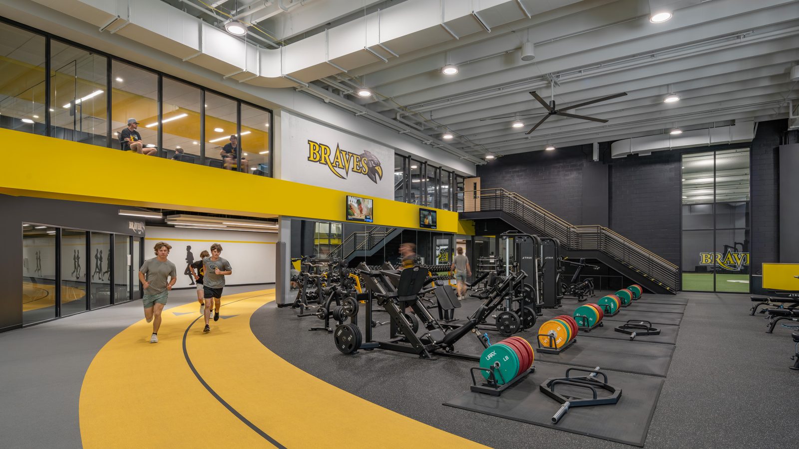 Fitness center with equipment including weights and exercise machines; students run on an indoor track.