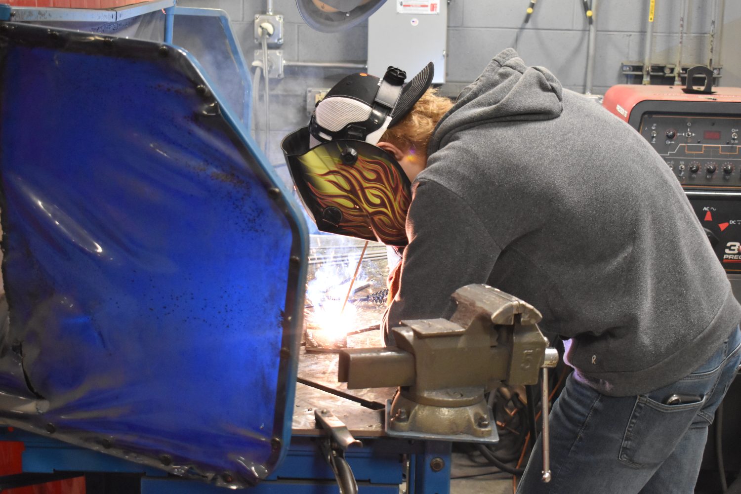 Person wearing welding hood and welding in booth with sparks.