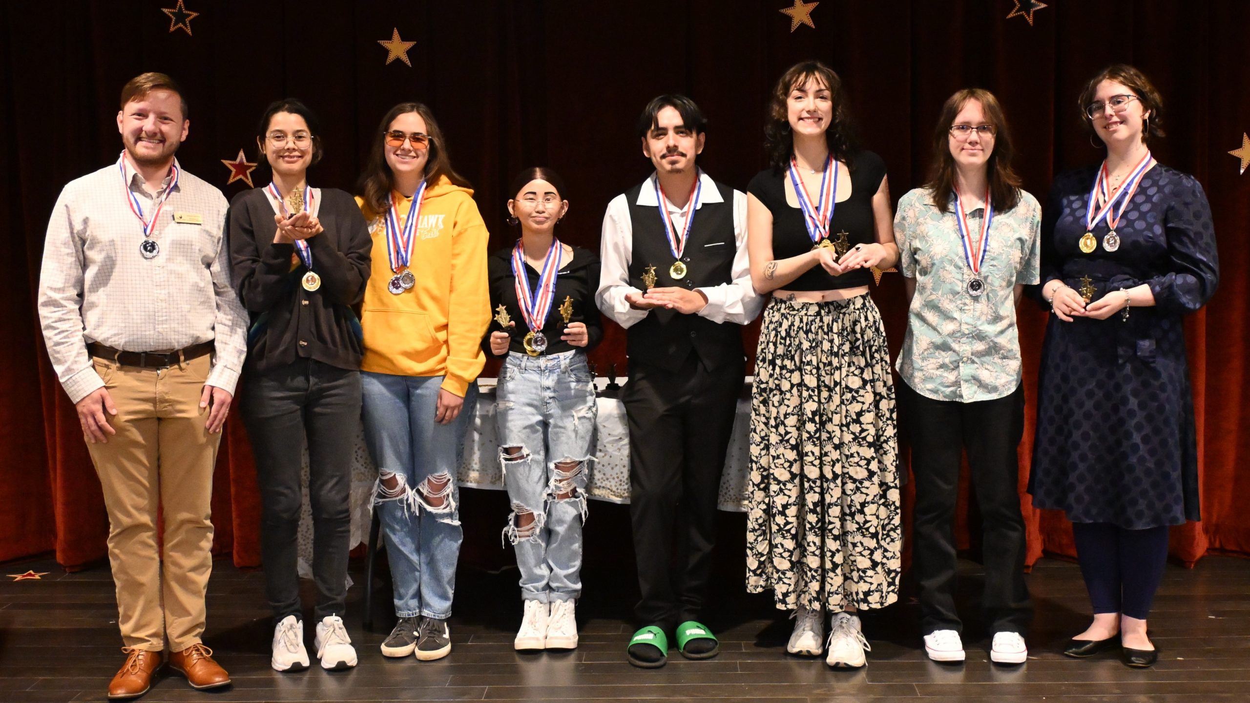 8 people standing on a stage with medals and awards.