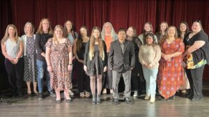 Group of 16 people standing on theatre stage