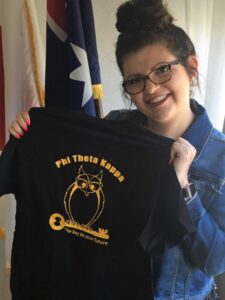 Smiling student holding up a phi theta kappa t-shirt