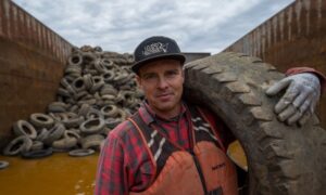 Man holding a tire with a pile of tires in the background