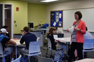 Associate professor walking in a classroom with college students at their desks