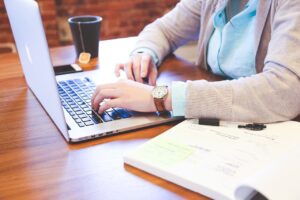 Hands typing on computer next to book on table
