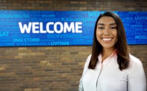 Smiling woman in front of a sign that says welcome