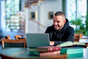 A smiling person sitting at a table with a laptop.