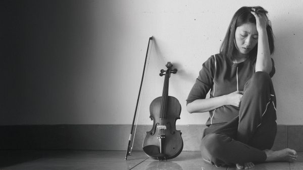 Overcoming performance anxiety - guest speaker Woman sitting on floor with hand on her head and back against wall with violin and bow next to her.
