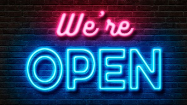 Brick wall with text we're open in neon lights.