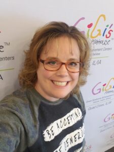 Woman smiling with gigi's playhouse logos behind her