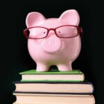 Pink piggy bank wearing red glasses on stack of books