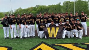 29 bhc baseball players on field smiling at camera with w banner
