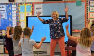 Music teacher and students holding their arms up while moving to the beat of a song