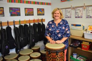 Music teacher behind a drum with drums and ukuleles behind her