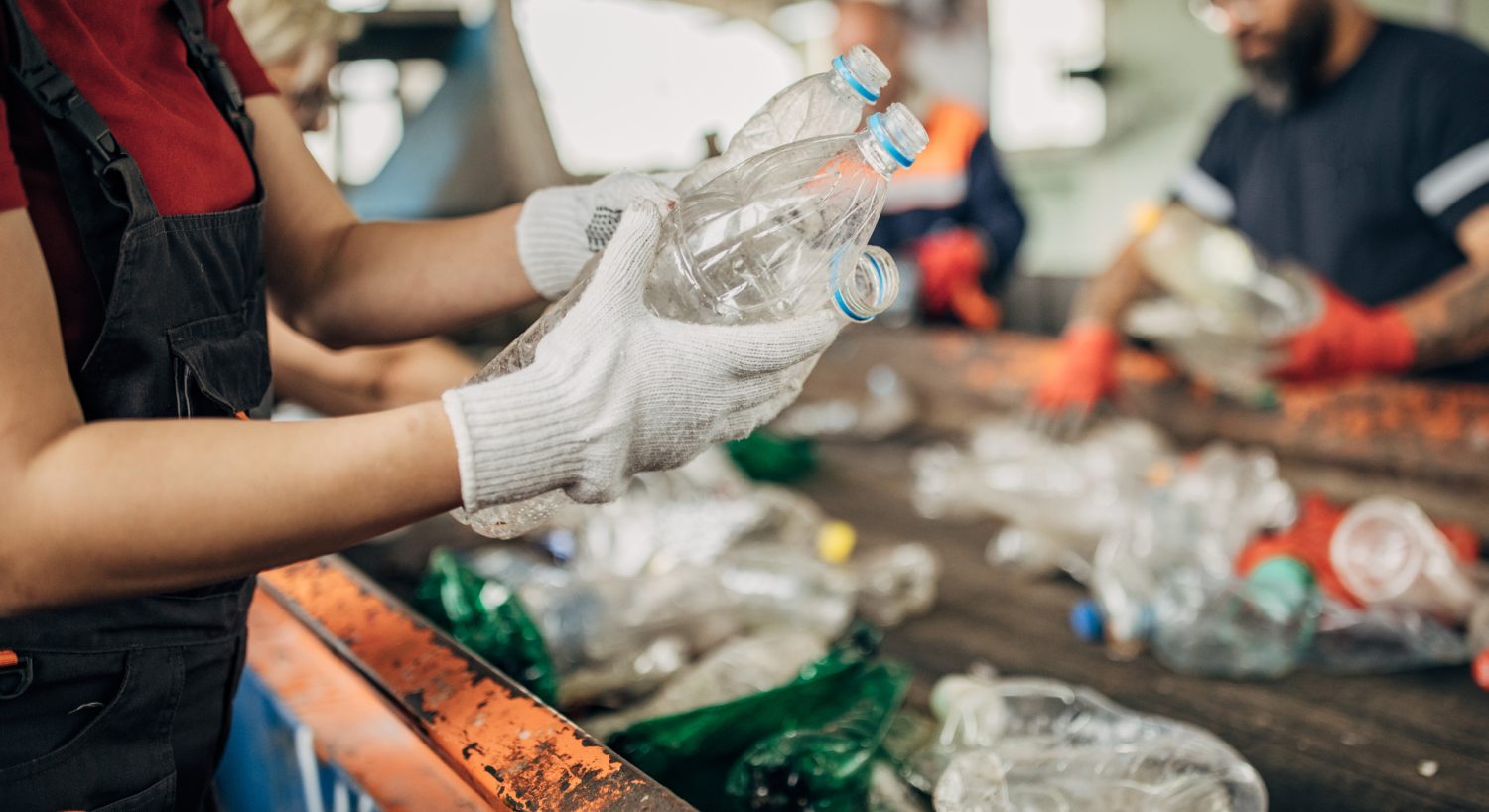 Quad-cities campus trash sort People sorting plastic bottles on conveyor belt.